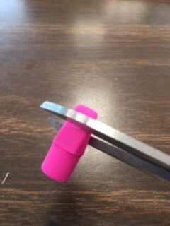 Scissors snipping the tip off of a pink cap eraser.